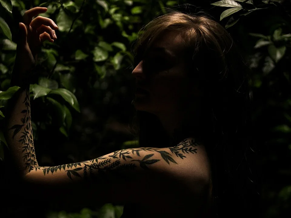 Arm mit fein gestochenem botanischem Tattoo zwischen Blättern